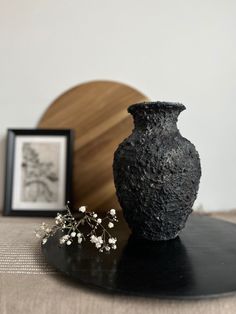 a black vase sitting on top of a table next to a framed photo and small white flowers