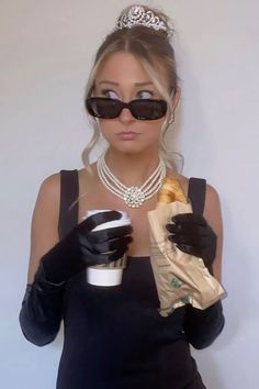 a woman wearing black gloves and holding a coffee cup in her right hand while wearing a tiara