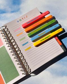 an open notebook with colored pencils sticking out of the pages and on top of it