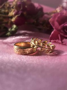 two gold wedding rings sitting on top of a pink table cloth next to flowers and petals