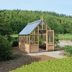 a small wooden greenhouse in the middle of a field with trees and bushes around it