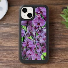 an iphone case with purple orchids on it sitting next to a cup and plant