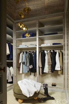 an open closet with clothes and shoes hanging on the wall, next to a footstool