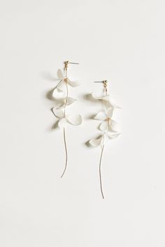 two white flowers hanging from the side of a pair of gold earwires on a white background