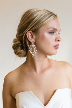 a woman in a white strapless dress with earrings on her head looking off to the side