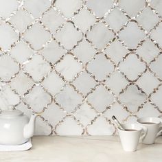 a white tea pot sitting on top of a counter next to a cup and saucer