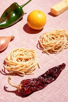 several different types of pasta and vegetables on a pink table cloth next to an orange