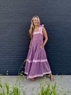 Meet Maisie, our newest cotton block print maxi dress in a Pink Posey print! She's full of sweet details like a tiered skirt, and contrasting striped banding. The bow straps are adjustable for the perfect fit, and it features a smocked back panel for comfort. Did we mention it has POCKETS!? Whether you're sipping lemonade on the porch or hitting up a summer wedding or soirée, this dress is a fun, versatile addition to your closet. Throw it on with sneakers or sandals, it's truly a go anywhere dr Tiered Cotton Maxi Dress For Garden Party, Cotton Tiered Skirt Maxi Dress For Garden Party, Cotton Tiered Maxi Dress For Garden Party, Cotton Maxi Dress With Tiered Skirt For Garden Party, Cotton Dress With Tie Straps And Tiered Skirt, Cotton Maxi Dress With Tie Straps, Cute Church Dresses, Pink And Blue Dress, Bow Straps