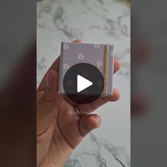 a hand holding a small gift box with a video playing on it