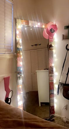 there is a mirror with lights on it and a pink hat hanging from the handle