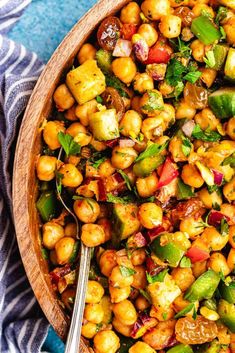 a wooden bowl filled with chickpeas and veggies next to a blue towel