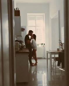 two people standing in a kitchen next to each other with one kissing the other's head