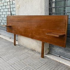 a wooden bench sitting on the side of a building next to a brick sidewalk and windows