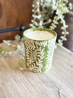 a green and white candle sitting on top of a wooden table next to a plant