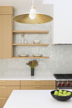 a kitchen with wooden cabinets and white counter tops, an island in the middle has green apples on it