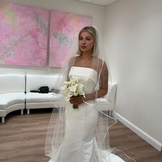 a woman in a white wedding dress holding a bouquet and standing next to a couch