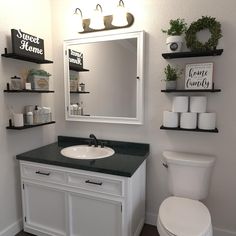 a white toilet sitting next to a bathroom sink under a mirror and shelves above it