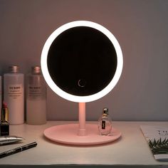 a round mirror sitting on top of a table next to a bottle of alcohol and a pen