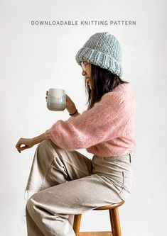 a woman sitting on a stool holding a coffee cup in one hand and a mug in the other