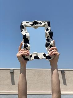 two hands holding up a square shaped object in front of a blue and white building