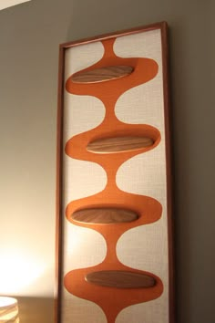 an orange and white painting hanging on the wall next to a table with a lamp