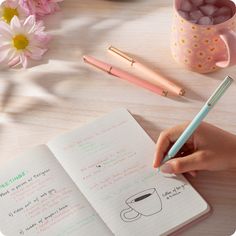 a person writing on a notebook with a pen and coffee mug in the background next to them