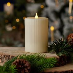 a white candle sitting on top of a wooden table next to pine cones and evergreen branches