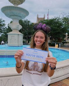 a woman holding up a sign in front of a fountain