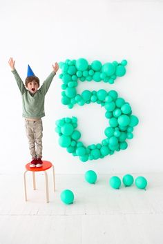 a young boy standing on top of a stool in front of a number 5 balloon wall