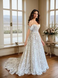 a woman standing in front of a window wearing a wedding dress with flowers on it