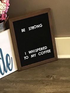 a sign that says be strong, i whispered to my coffee on it next to a potted plant