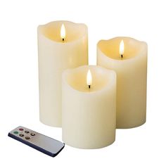 three white candles sitting next to a remote control on a marble counter top with a plant in the background