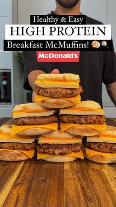 a man standing in front of a stack of cheeseburgers on top of a wooden table