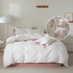 a bed with white sheets and pink bows on the comforter next to a lamp