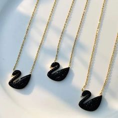 three black and gold necklaces on a white plate, one is shaped like a swan