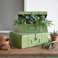 two green trunks with plants in them sitting on a table next to pots and gardening tools