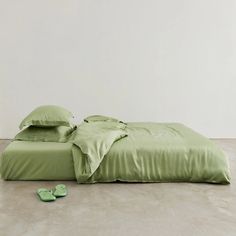 a bed with green sheets and slippers on the floor