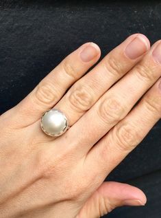 Choose your color and your ring size! This elegant and stately pearl ring is made from a beautiful and unique white cream 14mm Mabe South Sea AAA Pearl that has many hues including pink. The pearl has been set in sterling silver with a sterling silver ring band handmade from half dome wire. This ring has some height, the setting is almost 1/2 inch high. The white cream pearl is more matte than the other mabe pearls listed, but still has a luminescent quality that makes it captivating!Made to ord Elegant White Pearl Ring With Charm, Classic White Pearl Ring, Classic White Pearl Ring With Pearl Charm, Classic White Pearl Ring With Charm, Classic White Pearl Ring With Drop Detail, White Pearl Ring With Round Band, Elegant White Gold Pearl Ring With Bezel Setting, White Pearl Ring Fine Jewelry, Fine Jewelry White Pearl Ring With Round Band