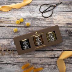 three jars of honey sitting on top of a wooden table next to scissors and flowers