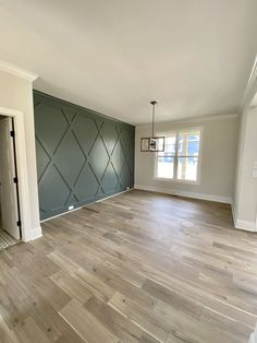 an empty living room with hard wood flooring and green accent wall behind the door