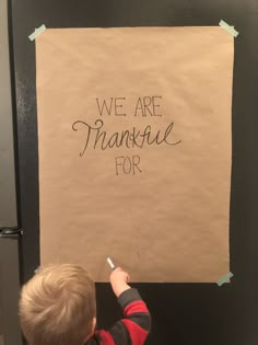 a little boy writing on a sign that says we are thanksgiving for