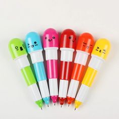 four pens with faces drawn on them are lined up in a row and each has different colors