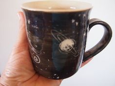 a hand holding a black and white coffee cup with an image of the planet on it