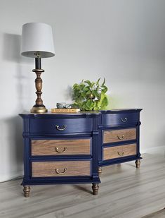 a blue dresser with two drawers and a lamp on top of it next to a white wall