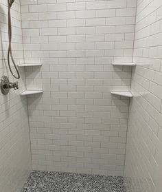 a walk in shower sitting next to a white tiled wall with shelves on each side