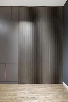 an empty room with grey walls and wooden flooring in front of a wall that has vertical slats on it