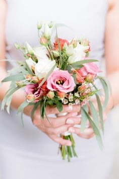 a woman holding a bouquet of pink and white flowers with greenery in her hands