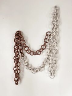 two pieces of chain hanging from the side of a white wall, one with brown chains on it