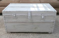 an old white trunk is sitting on the carpet in front of a couch and coffee table