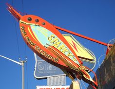 a large neon sign hanging from the side of a building in front of a blue sky